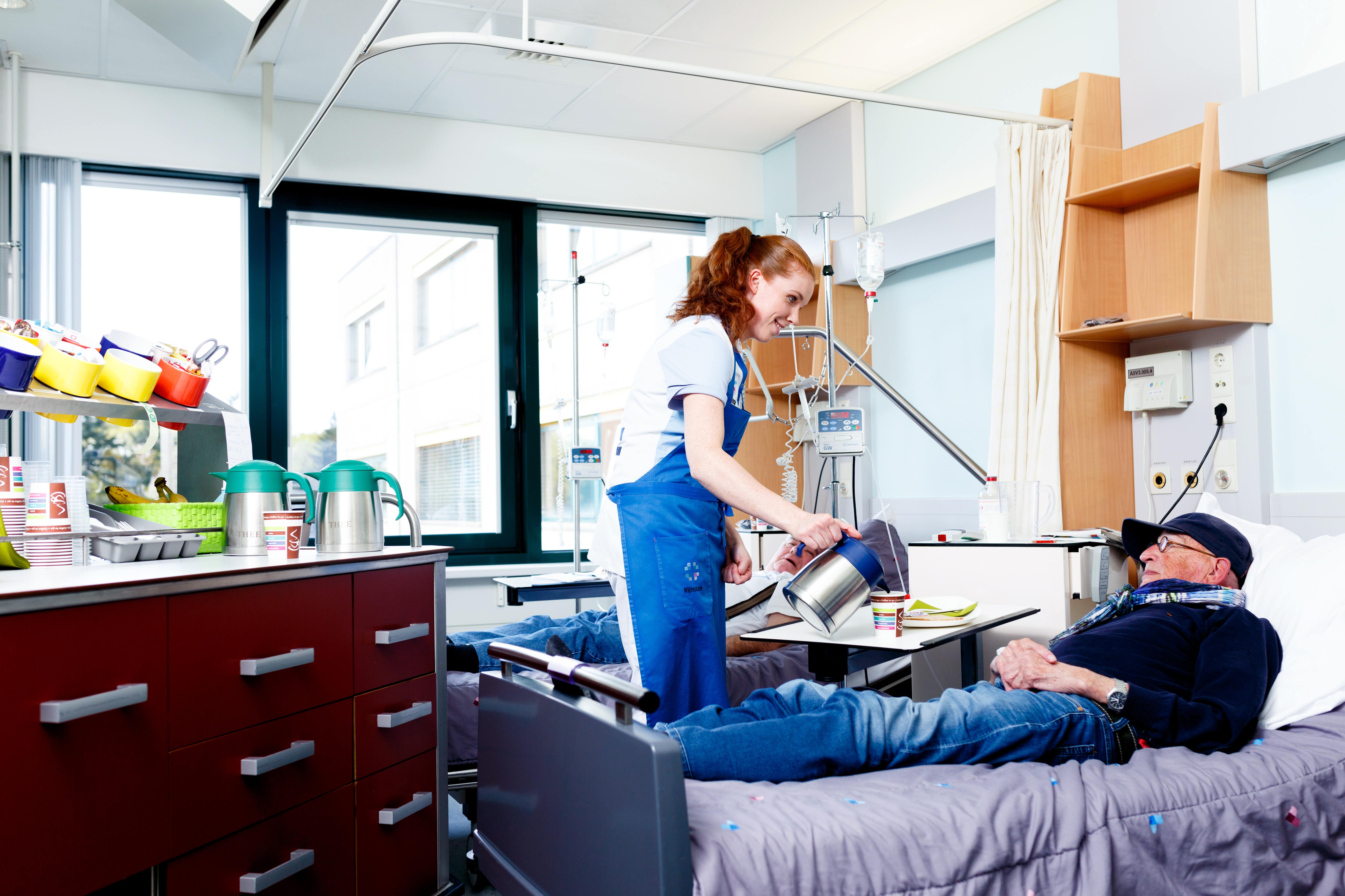 Serviceassistent staat aan het bed van een patiënt en schenkt koffie in